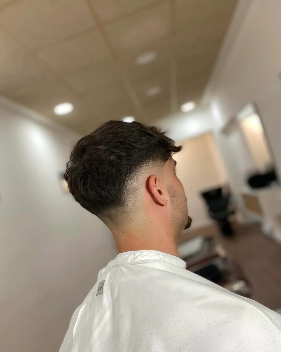 Degradado en los lados y la nuca, con el pelo castaño y ondulado arriba