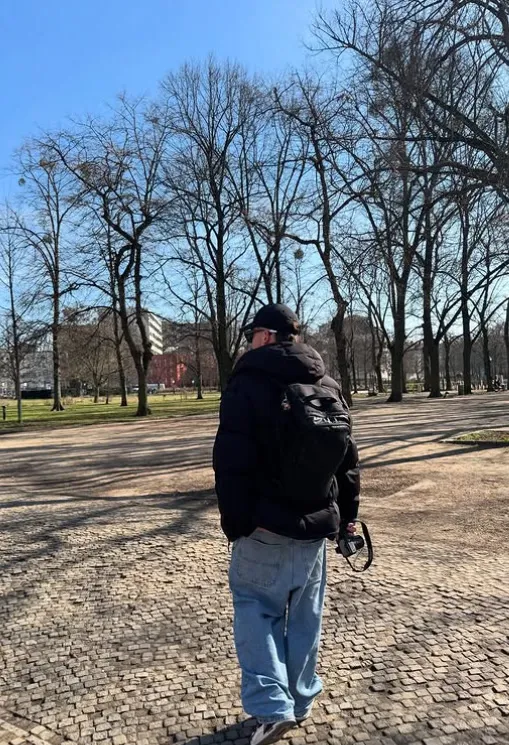 Xavier Zapata Cantalejos, de espaldas, paseando por un parque con una cámara de fotos en la mano